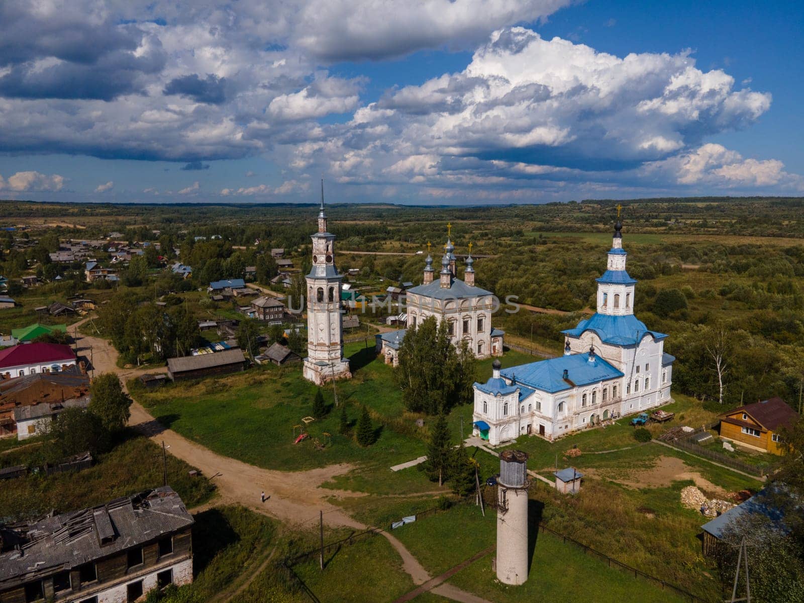 Aerial view of aged churches and chantry on meadow against dwelling houses under cloudy blue sky in region of Kirov Russia