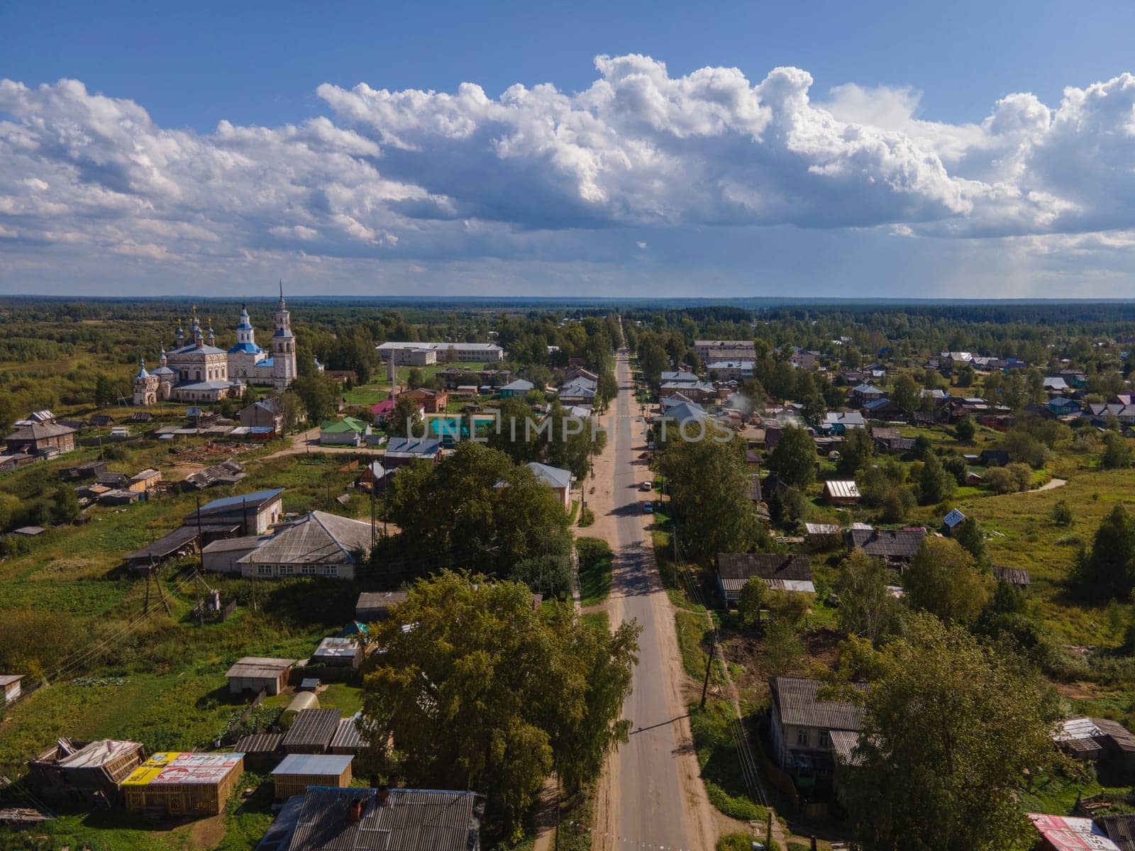 Aerial view of straight road going through countryside with residential buildings under blue cloudy sky in summer