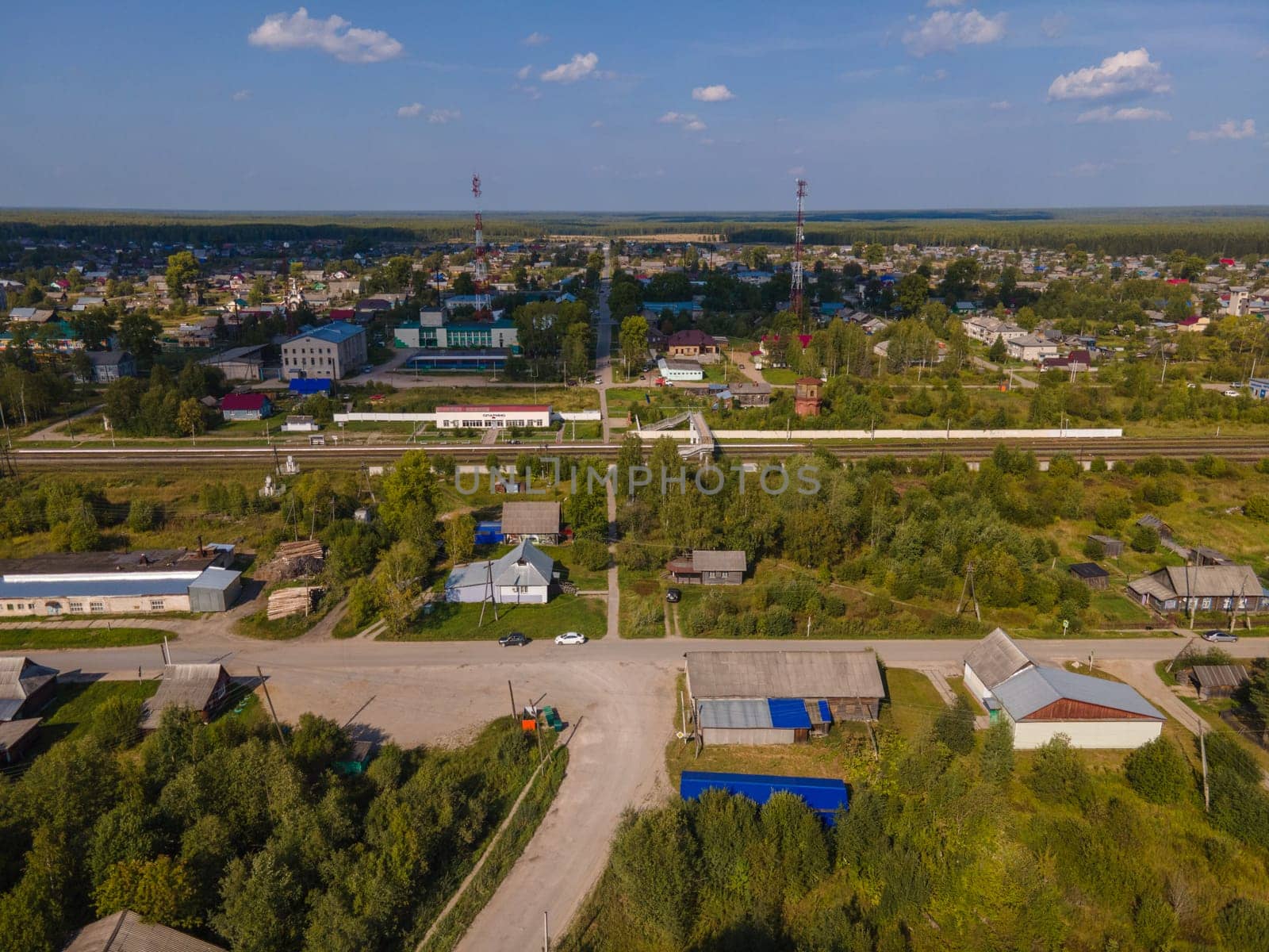 Drone view of roadway between trees and dwelling buildings under cloudy blue sky in region of Kirov Russia