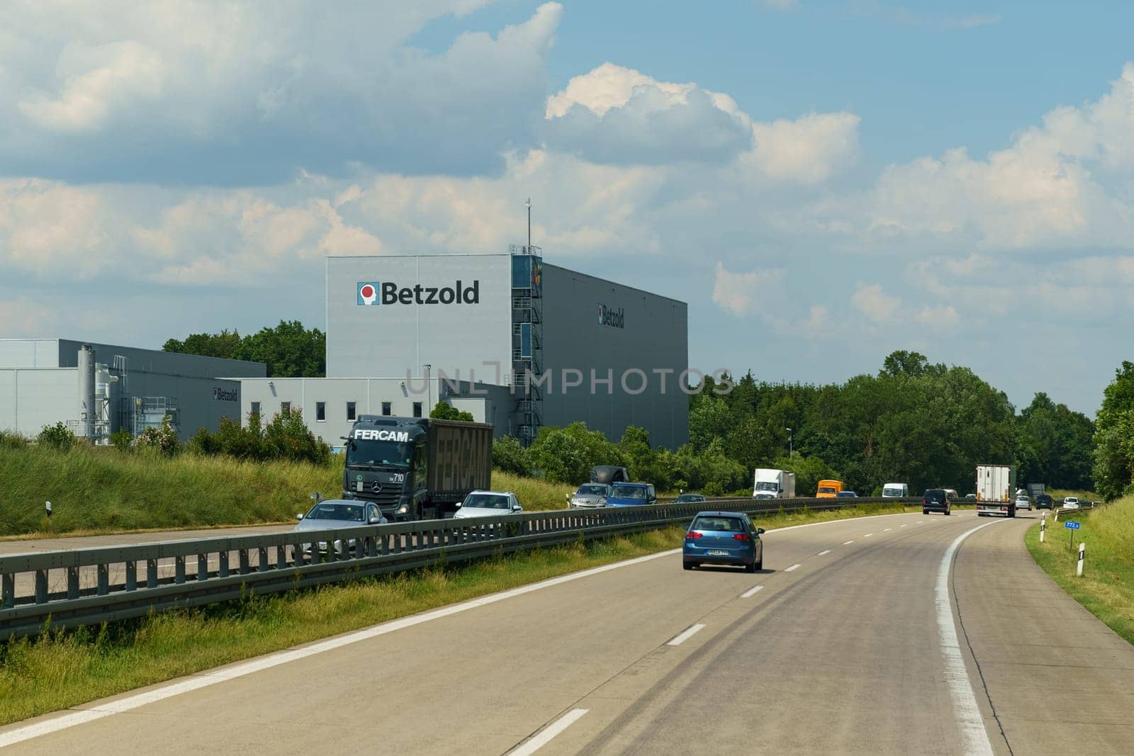 Vehicles traveling on a highway under clear skies, with a large Betzold sign visible on an adjacent building.