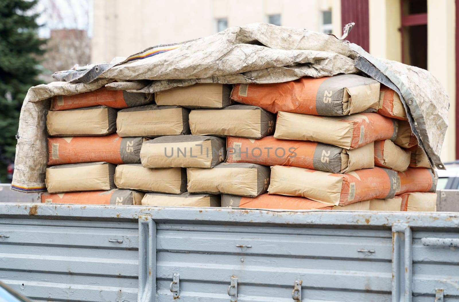 A pickup truck bed is filled with stacked cement bags, indicating ongoing construction work at a site.