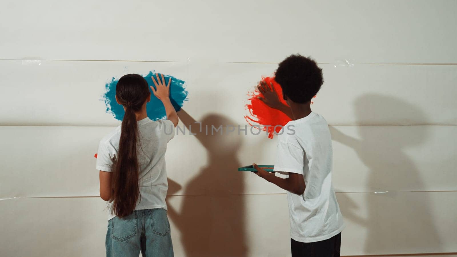 Diverse happy highschool girl and african boy paint the wall with water color in red and blue or contrast color by using their hands in art lesson. Colorful. Creative activity concept. Edification.