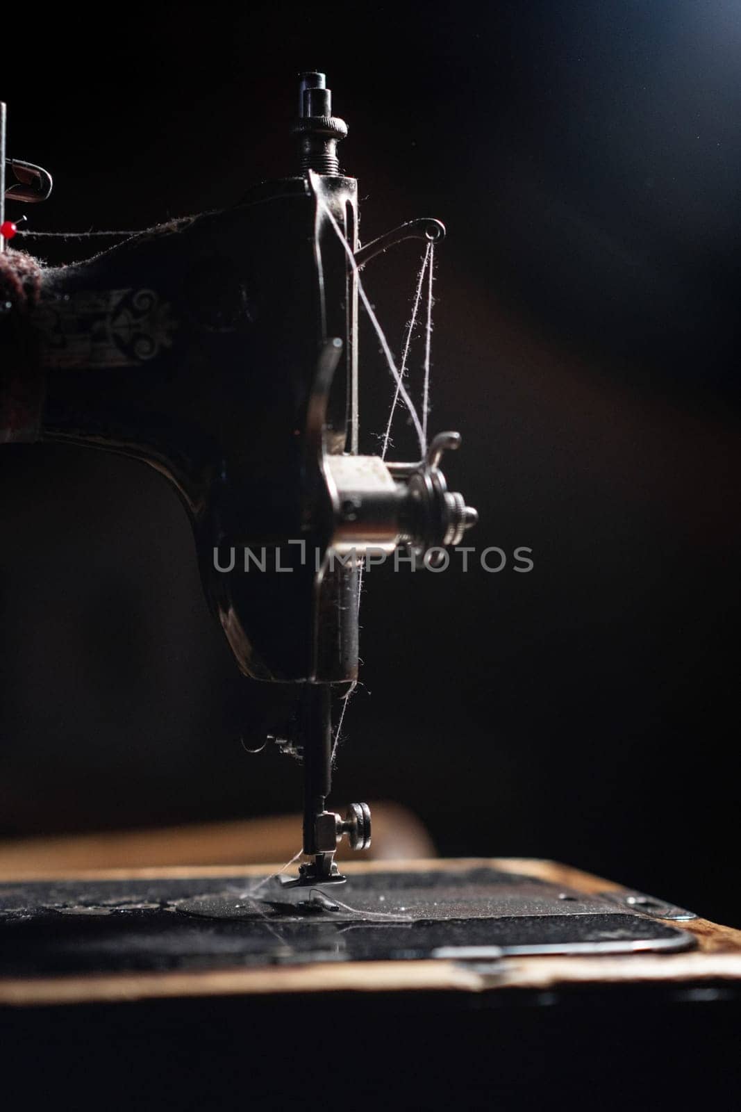 An old sewing machine stands on the table at home ready to work and sew. Classic retro style manual sewing machine ready for sewing work. The machine is old style made of metal with floral patterns