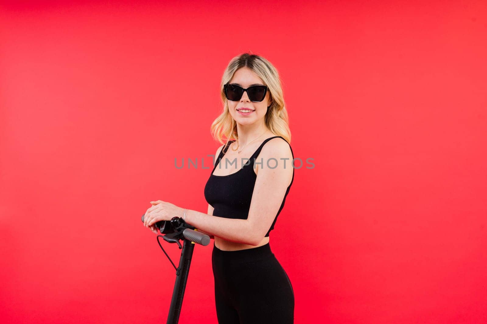 Blonde woman on red white background sitting on electro scooter and resting, copy space by Zelenin