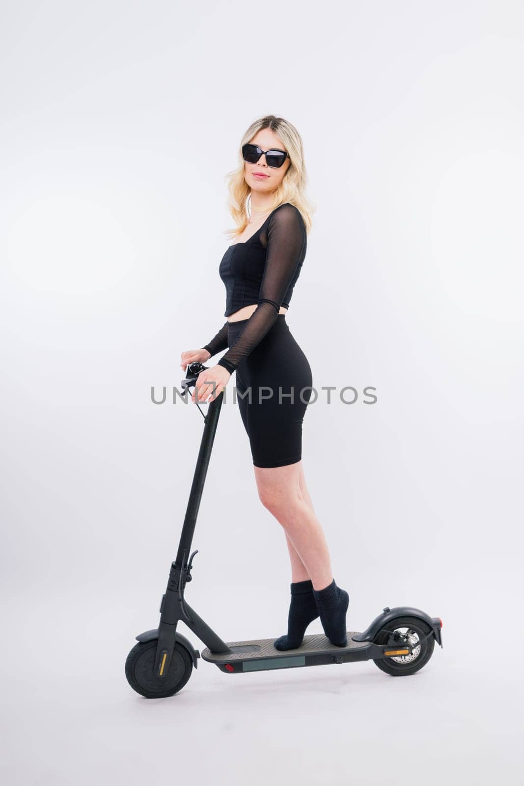 Blonde woman on red white background sitting on electro scooter and resting, copy space by Zelenin