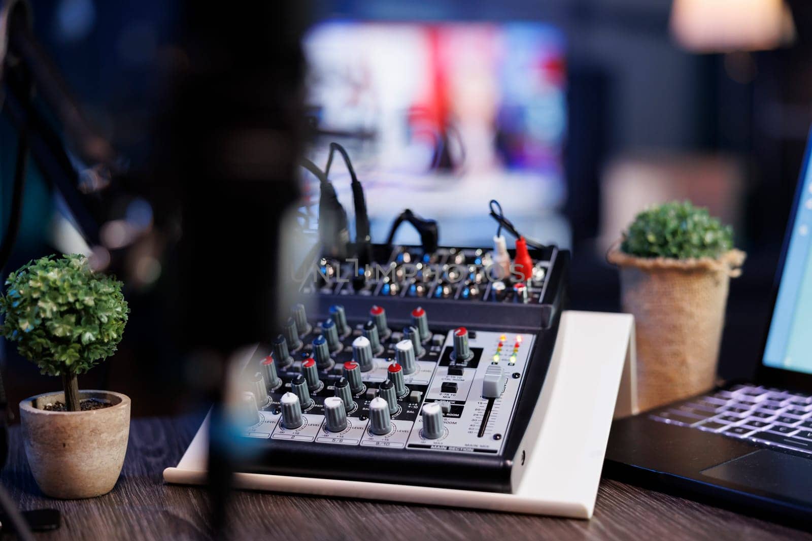 Selective focus on laptop keyboard and audio mixer knobs on a podcasting desk in the home studio. Detailed view of buttons on professional sound equipment used for live internet broadcasts.