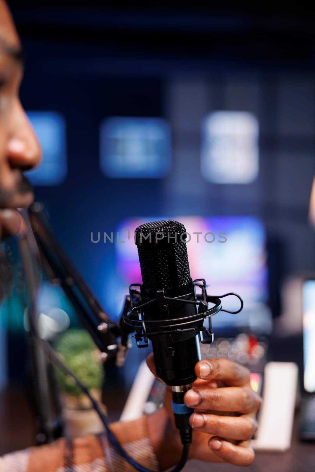 Male presenter recording live talk show using professional audio equipment at home. African american man speaking into microphone doing an online production, creating a podcast episode.