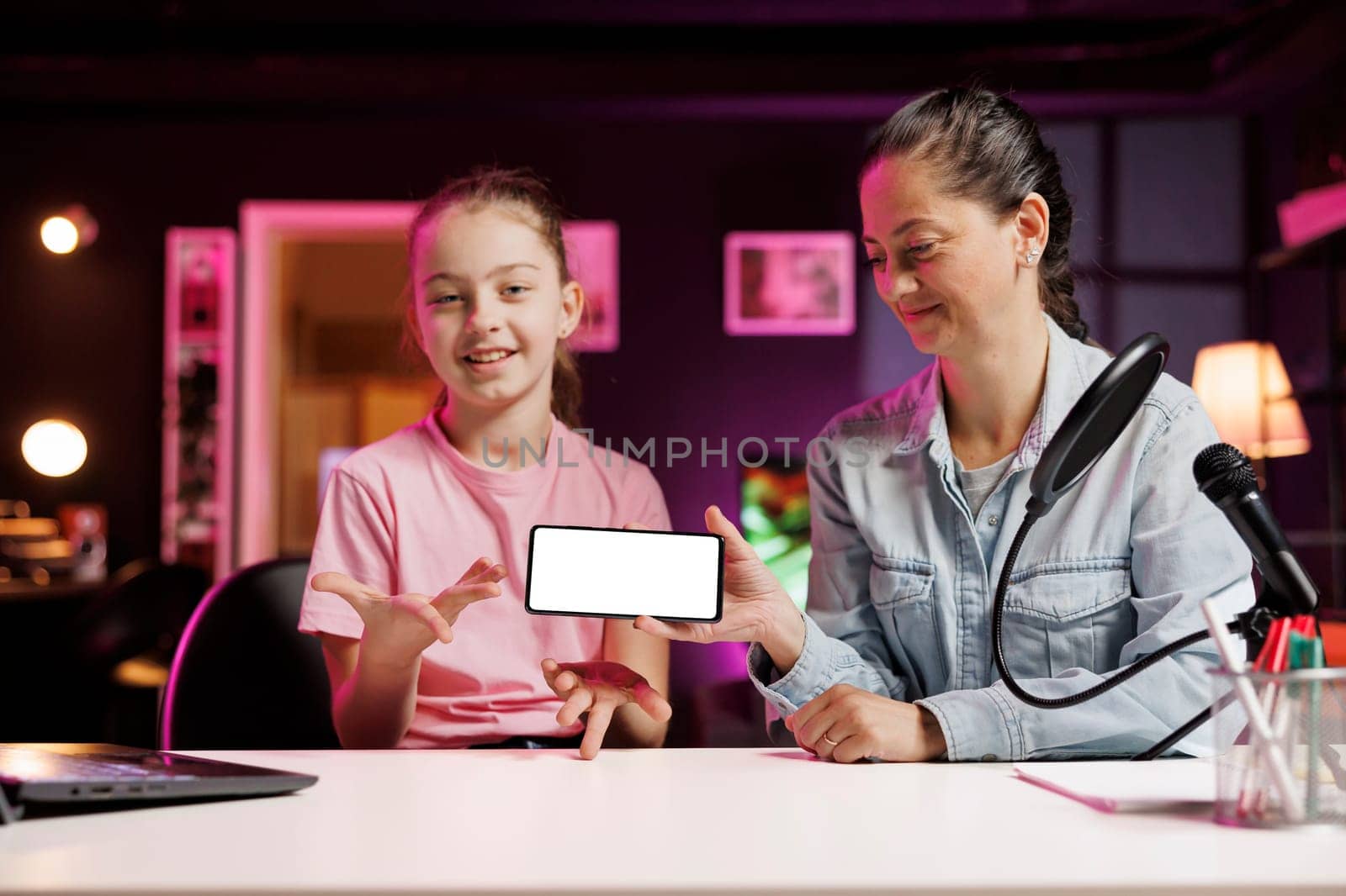 Daughter and mom being sponsored by partnering brand to do mockup mobile phone unboxing content. Small child and parent do influencer marketing, doing isolated screen smartphone product placement