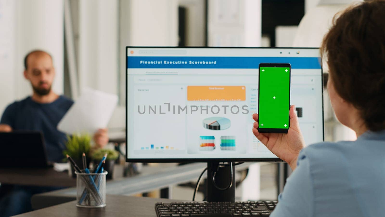 Adult holding phone with greenscreen in coworking space at office. Businesswoman working with smartphone showing isolated mockup template, analyzing chromakey layout on gadget. Tripod shot.