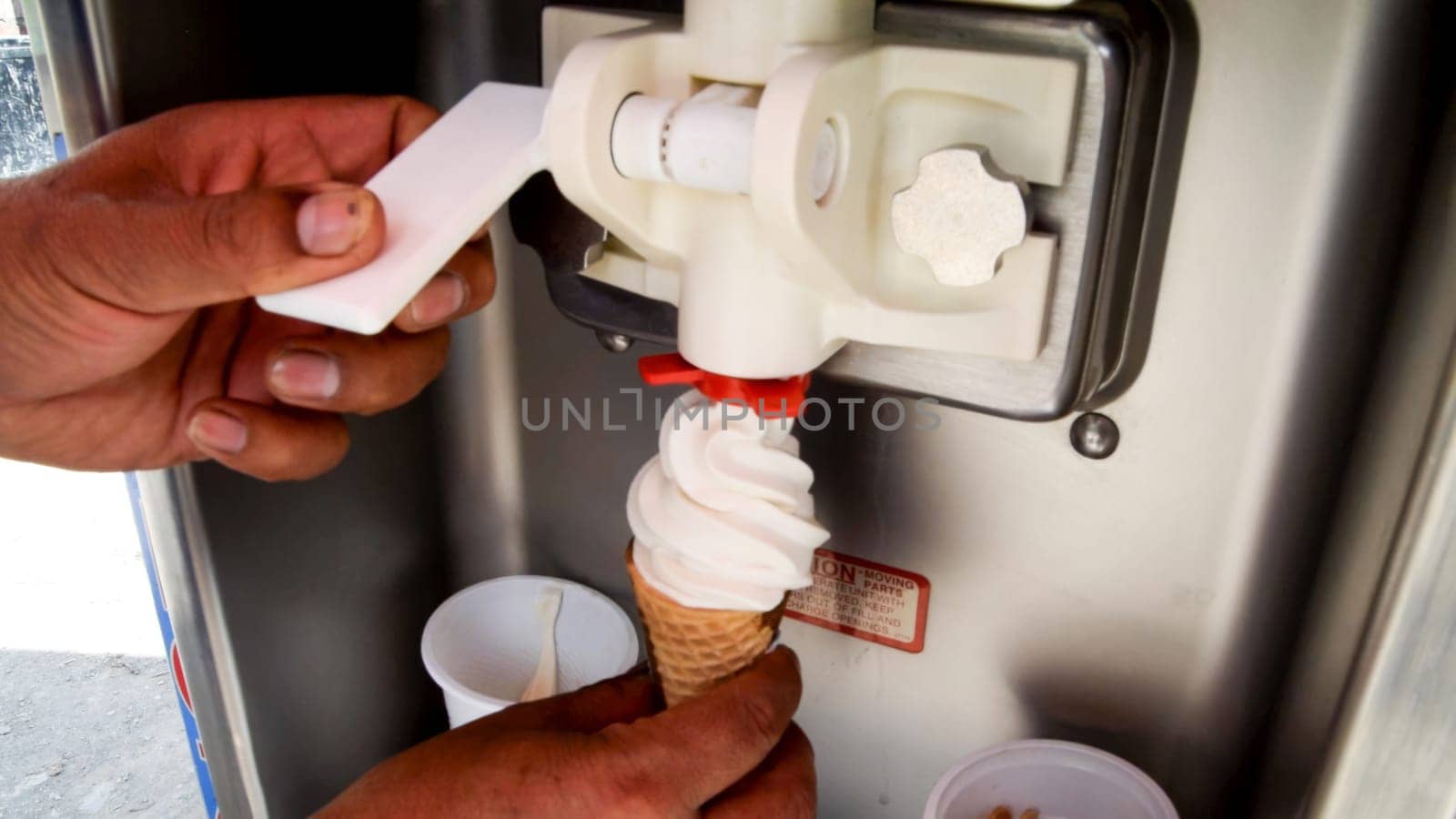 Hands operating a soft serve machine and filling a cone with fresh, creamy ice cream