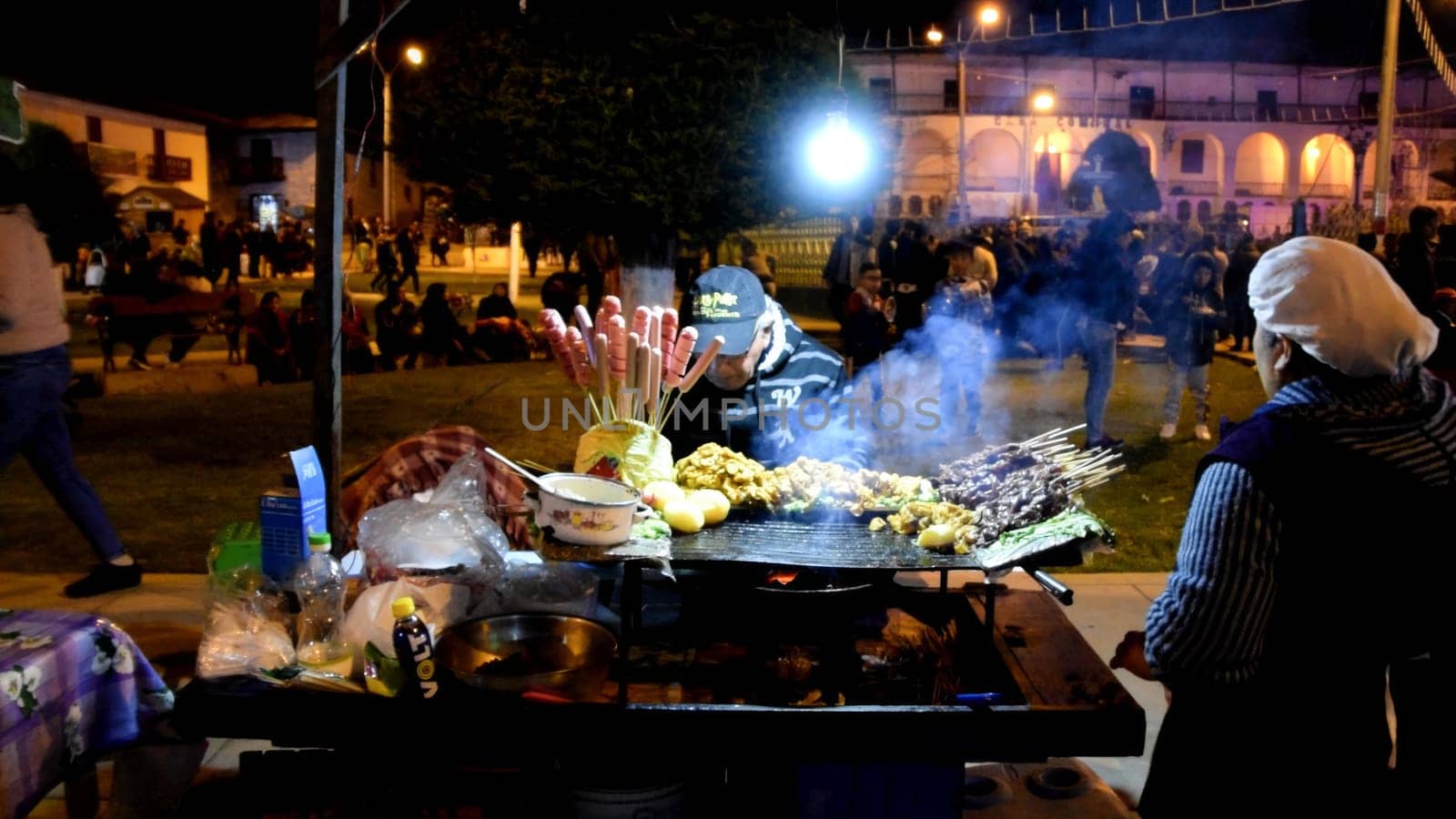 Lima, Peru - September 7, 2019 : Local street vendor grills delicious snacks at a bustling night market, surrounded by customers, city of Canta located north of Lima - Peru