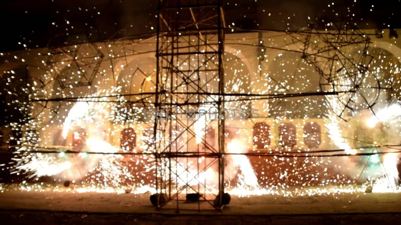 Vibrant fireworks illuminate a scaffold at night, creating a stunning light show