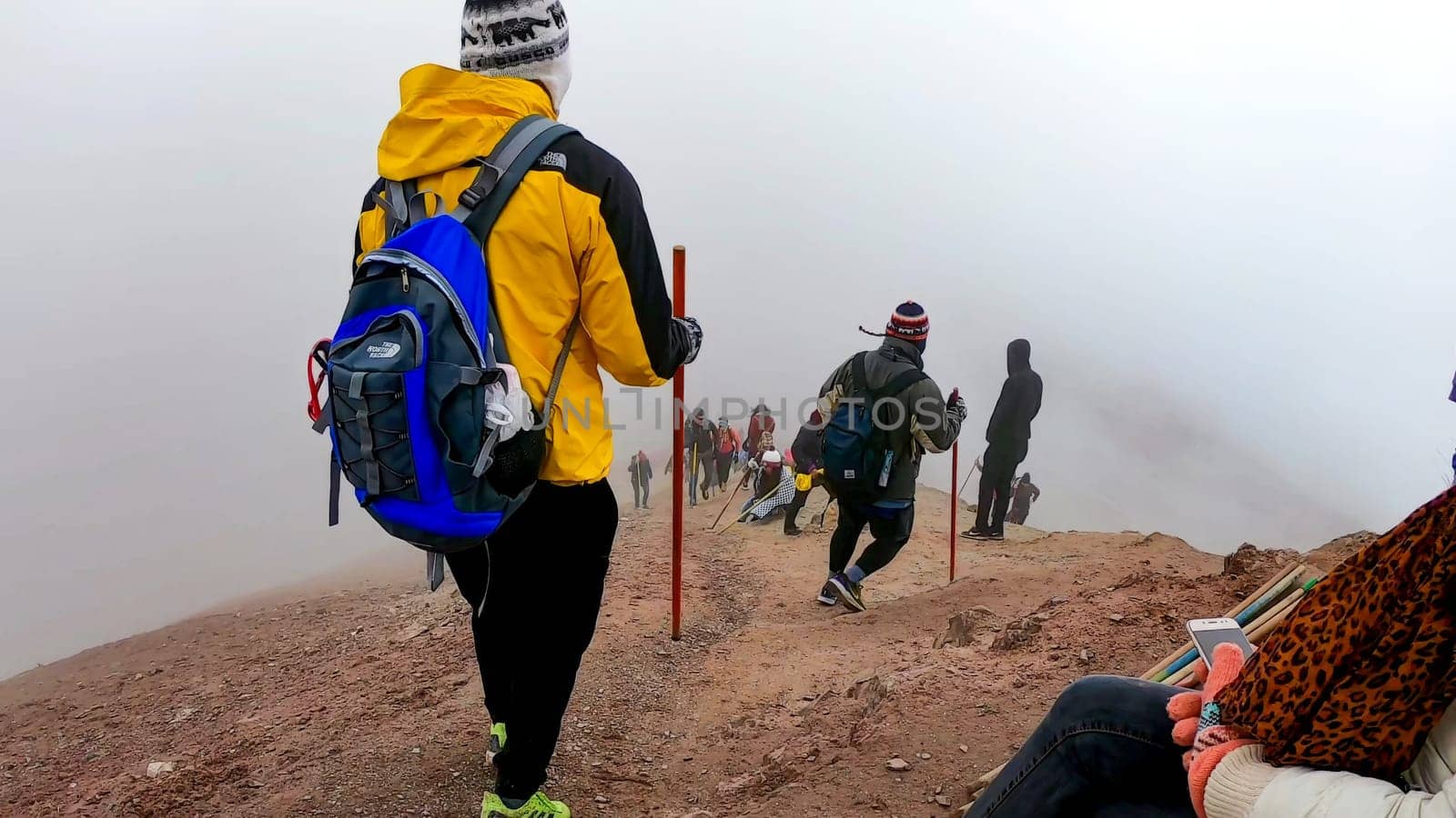Cusco, Peru - February 9 2019 : Group of hikers on a foggy path up a mountain equipped with walking sticks and backpacks, the Rainbow mountain in Cusco - Peru
