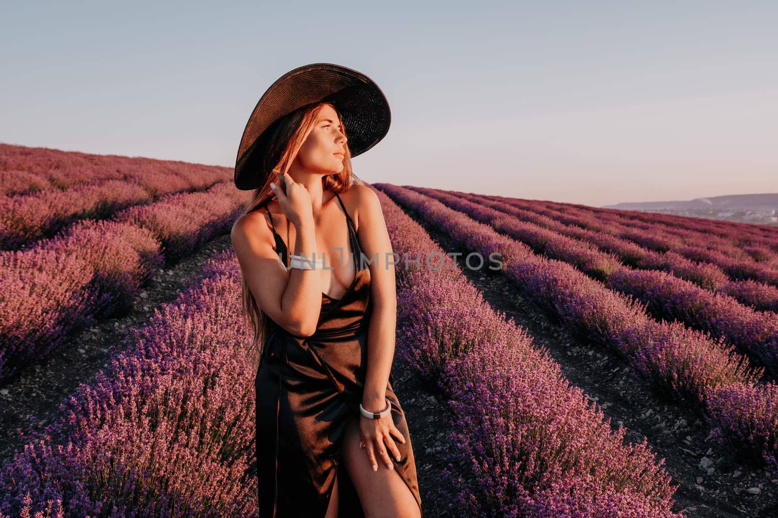 Woman lavender field. Happy carefree woman in black dress and hat with large brim walking in a lavender field during sunset. Perfect for inspirational and warm concepts in travel and wanderlust. by panophotograph