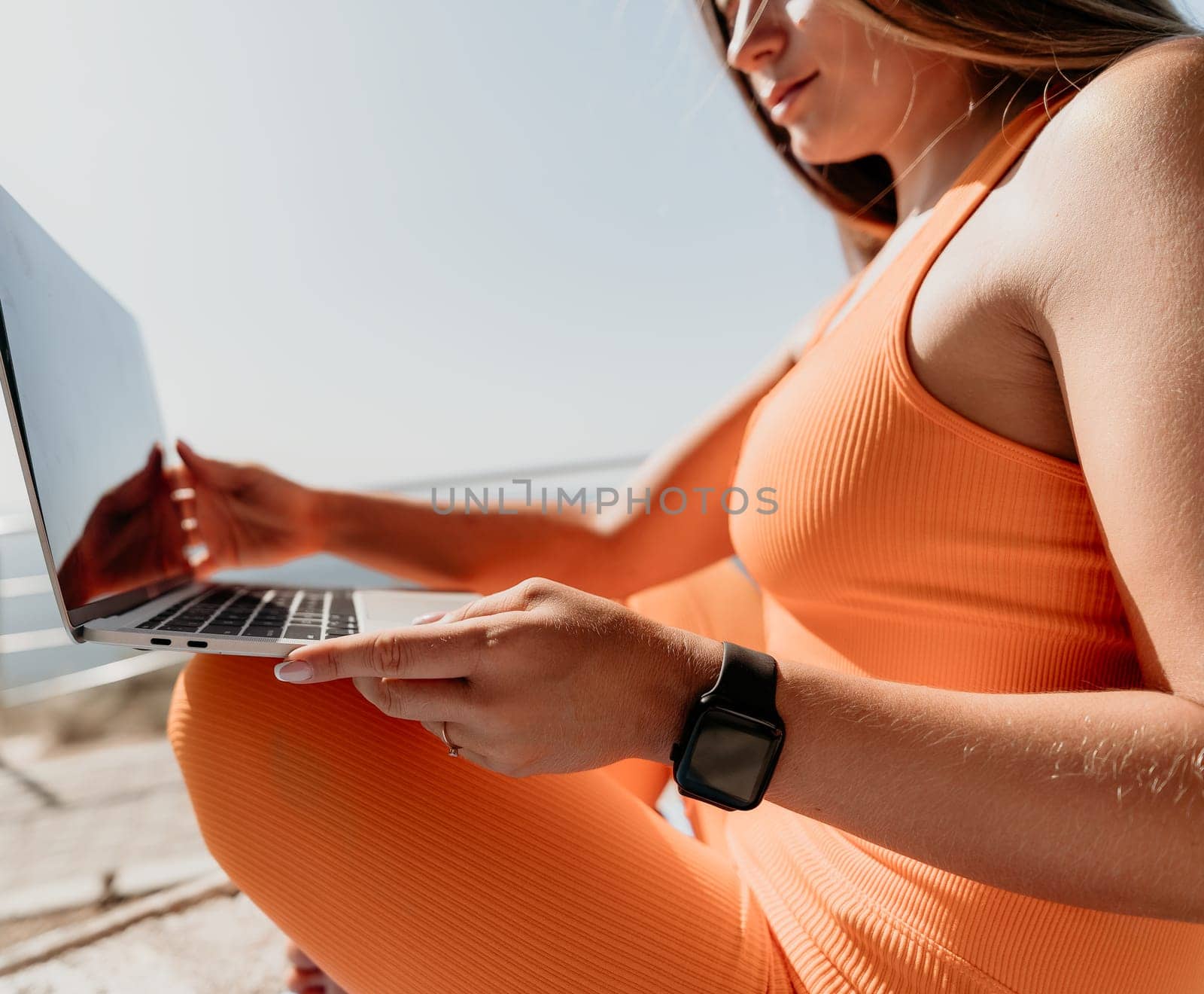 Woman laptop sea. Working remotely on seashore. Happy successful woman female freelancer working on laptop by the sea at sunset, makes a business transaction online. Freelance, remote work on vacation by panophotograph