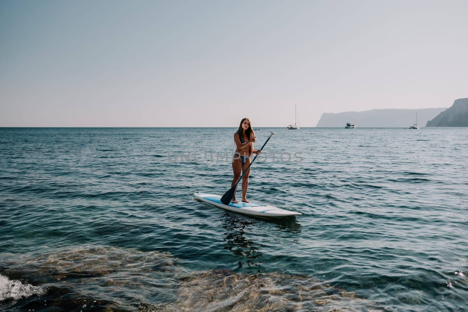 Close up shot of happy young caucasian woman looking at camera and smiling. Cute woman portrait in bikini posing on a volcanic rock high above the sea