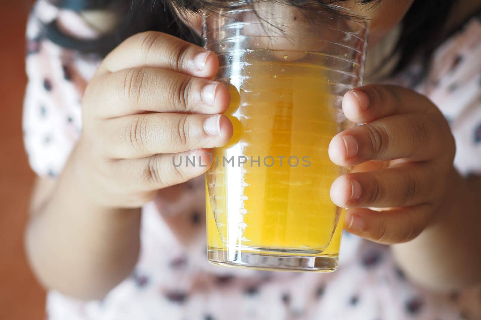 child hand holding a glass of orange juice .