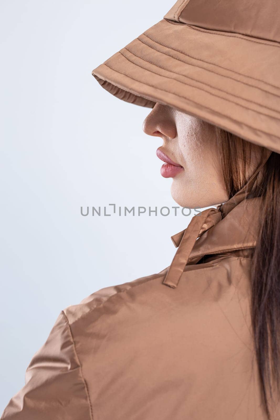 Woman in elegant brown raincoat and hat, looking contemplative. Radiates sophistication and style, with a hint of mystery.