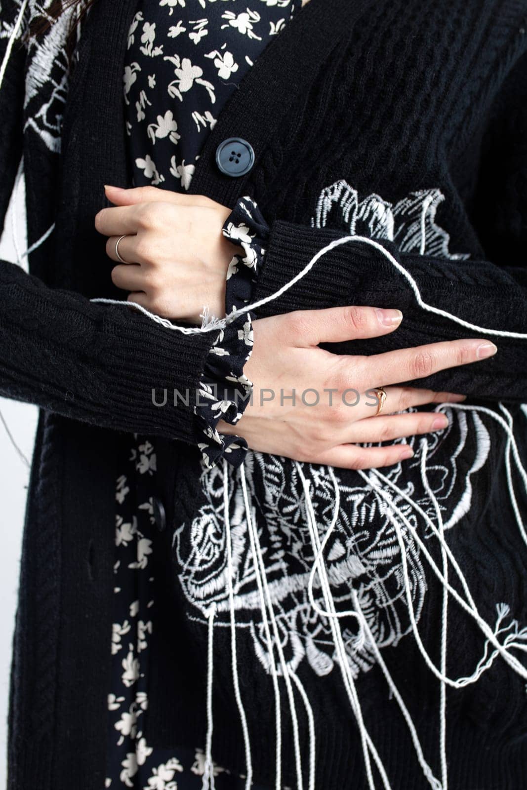 A young woman in a black cardigan with white floral embroidery, cropped style, holding it closed. Worn over a black blouse.