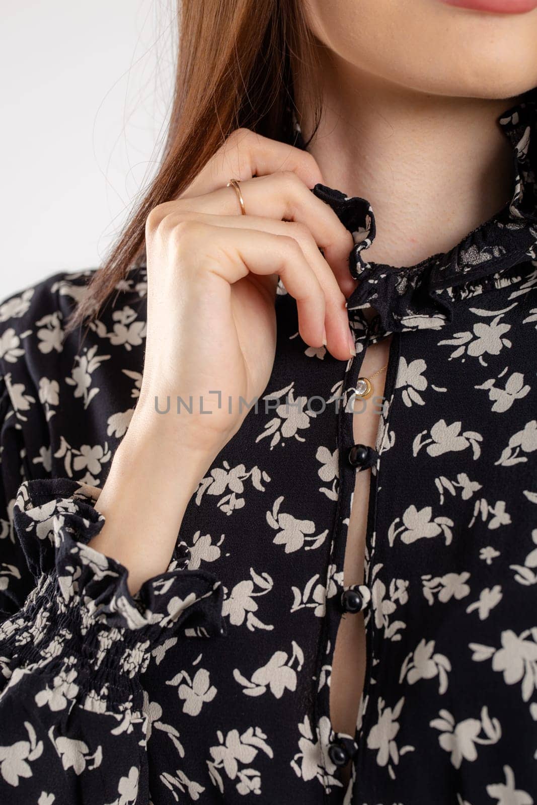 Portrait of a woman with long brown hair in a black floral blouse, looking serious at the camera with elegant style.