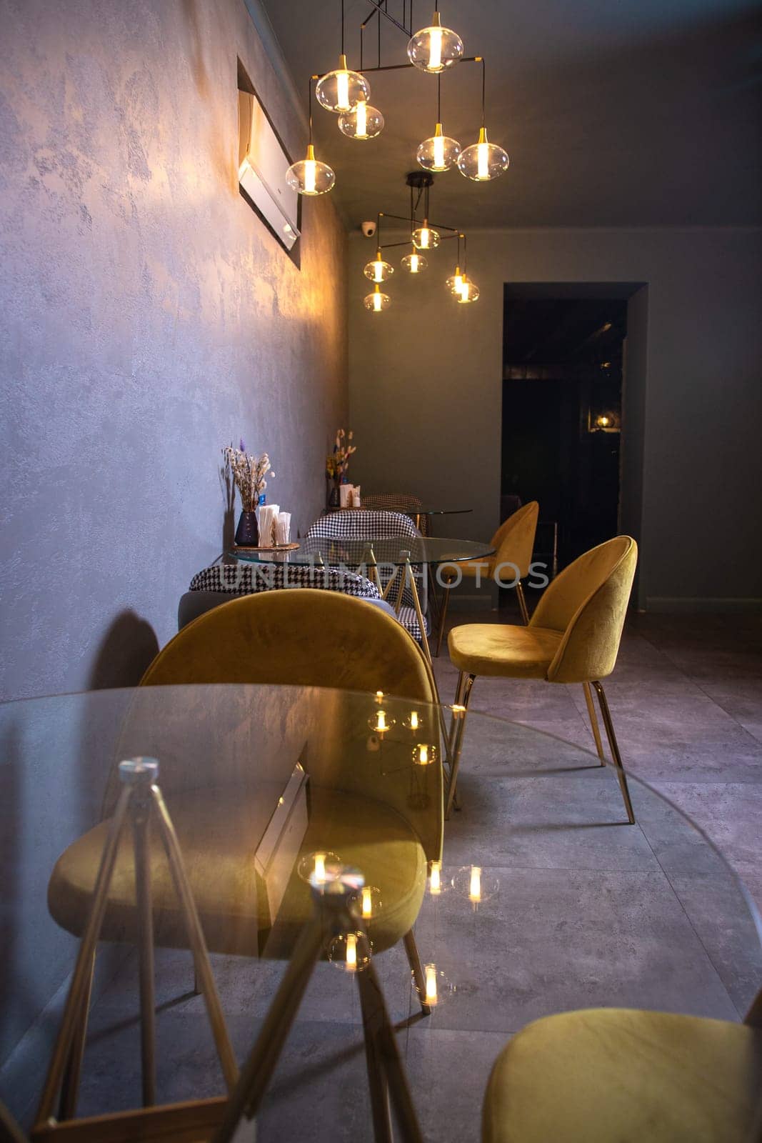 Cozy restaurant interior with glass tables, yellow chairs, textured walls, and pendant lights hanging from the ceiling.