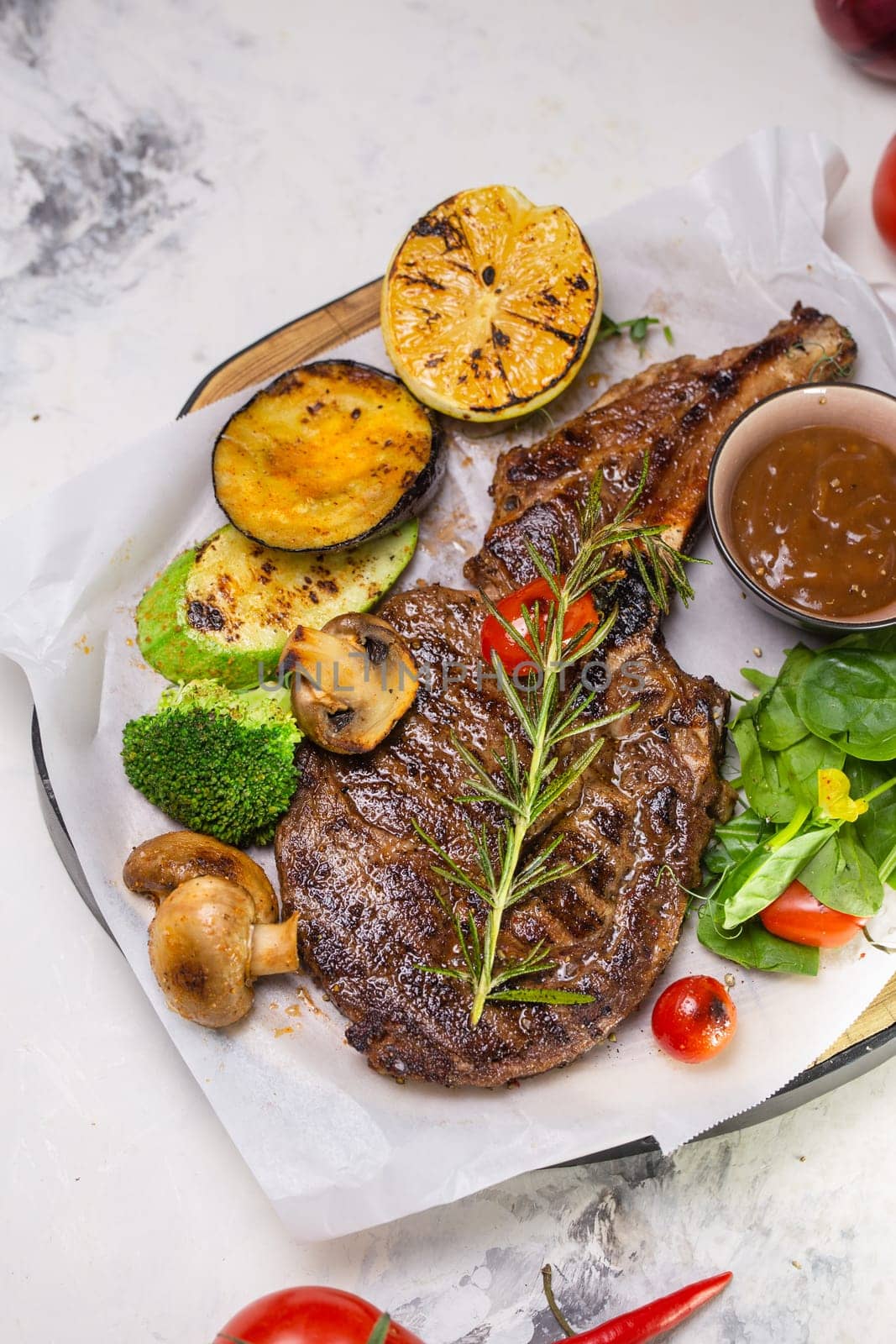 A juicy and tender grilled steak is served with a variety of roasted vegetables and topped with a sprig of rosemary.