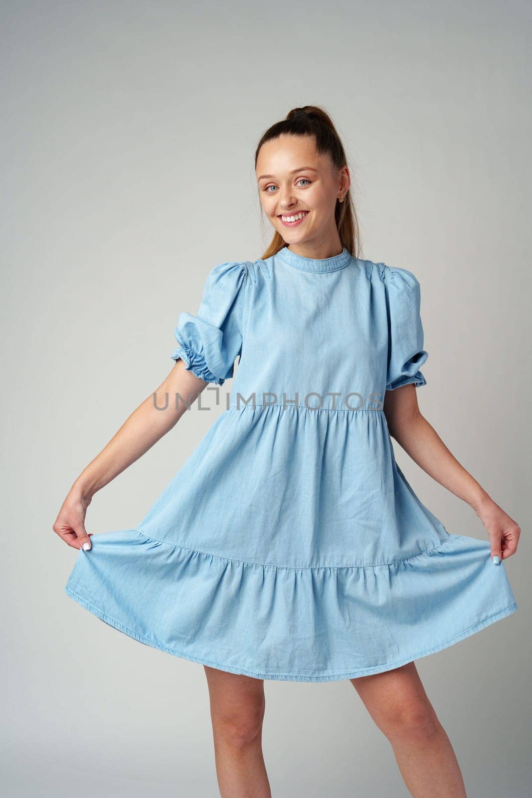 Young happy smiling woman in a light blue dress on a gray background close up