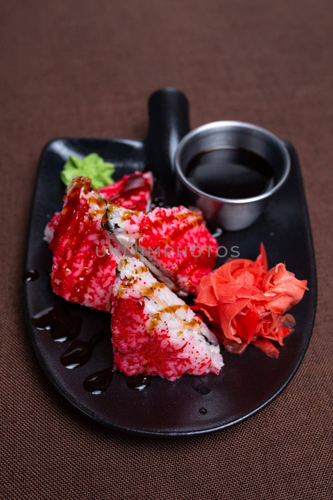 A closeup of a plate of sushi rolls with caviar, wasabi, and soy sauce. The sushi is arranged in a circle on the plate.