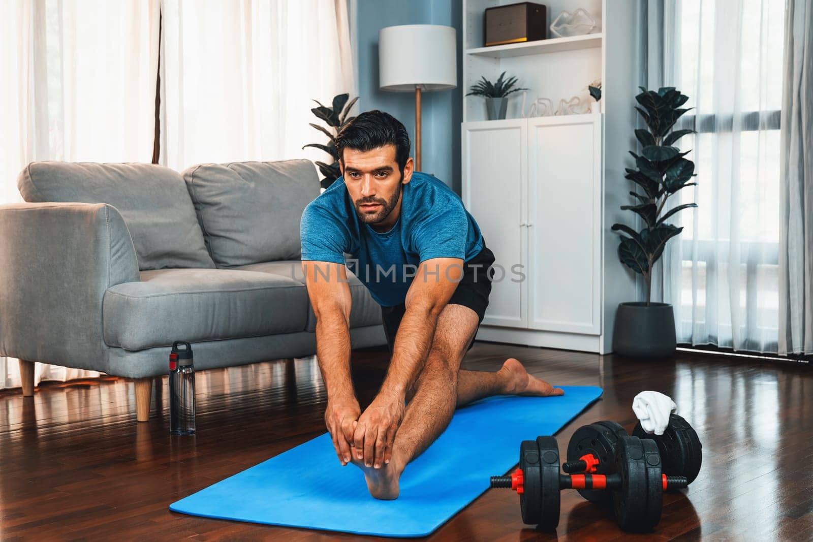 Athletic and sporty man doing warmup and stretching before home body workout exercise session for fit physique and healthy sport lifestyle at home. Gaiety home exercise workout training concept.
