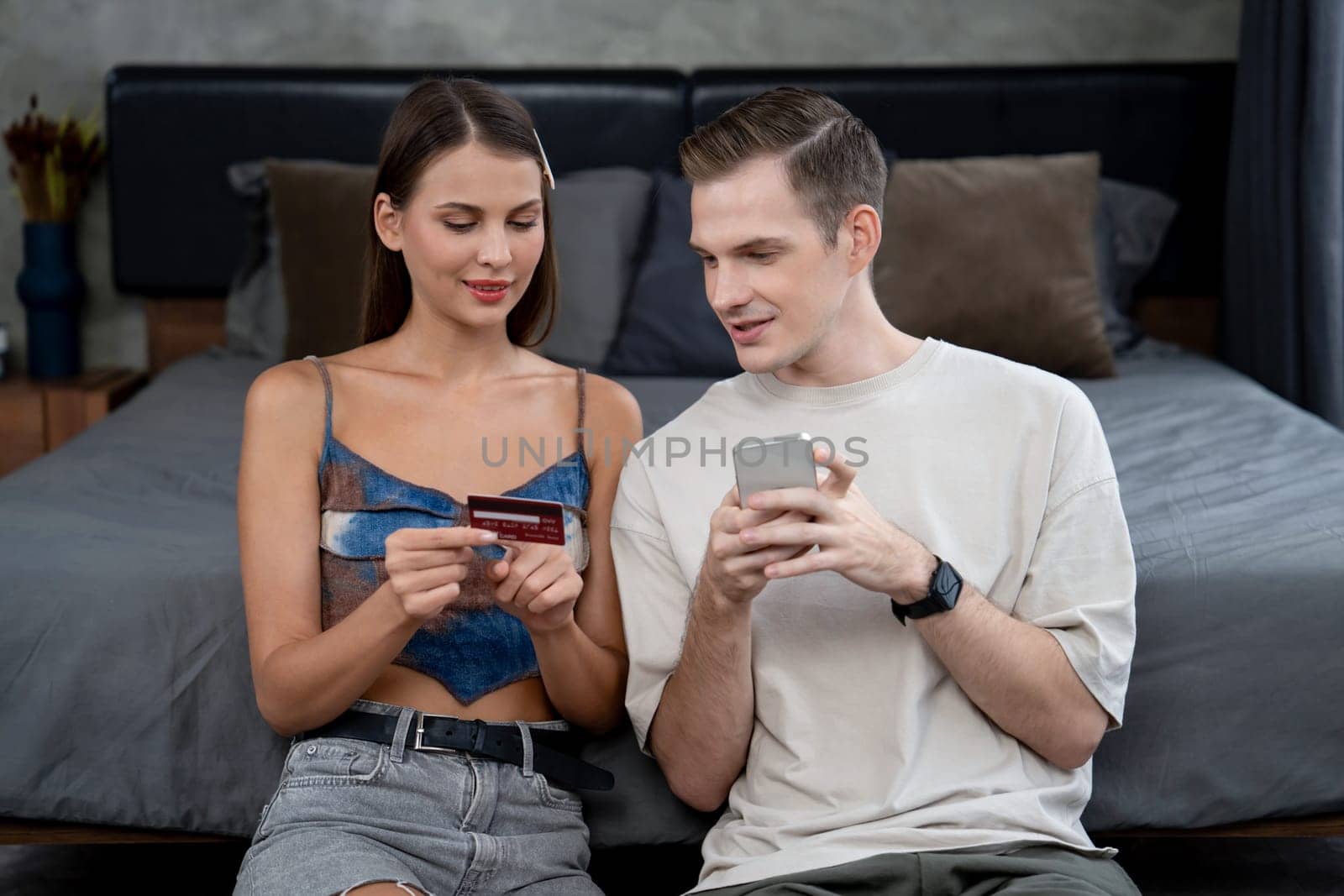 Young couple sit in the bed room using online payment app. Unveiling by biancoblue