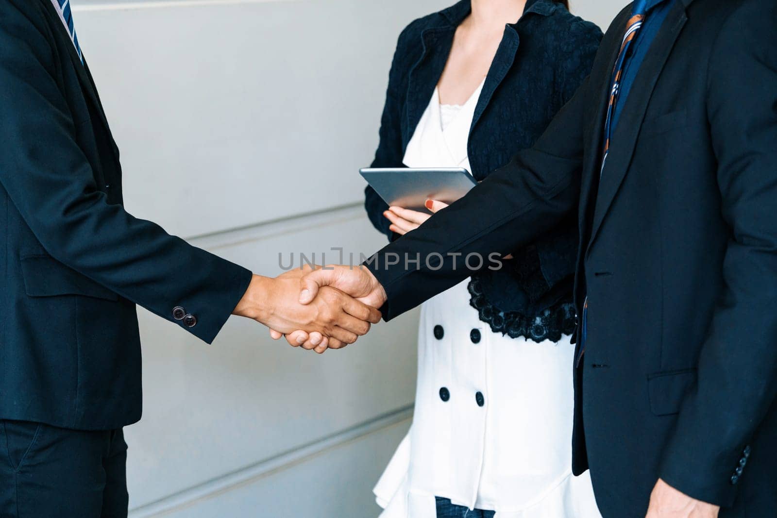 Business people agreement concept. Businessman do handshake with another businessman in the office meeting room. Young Asian secretary lady stands beside them. uds