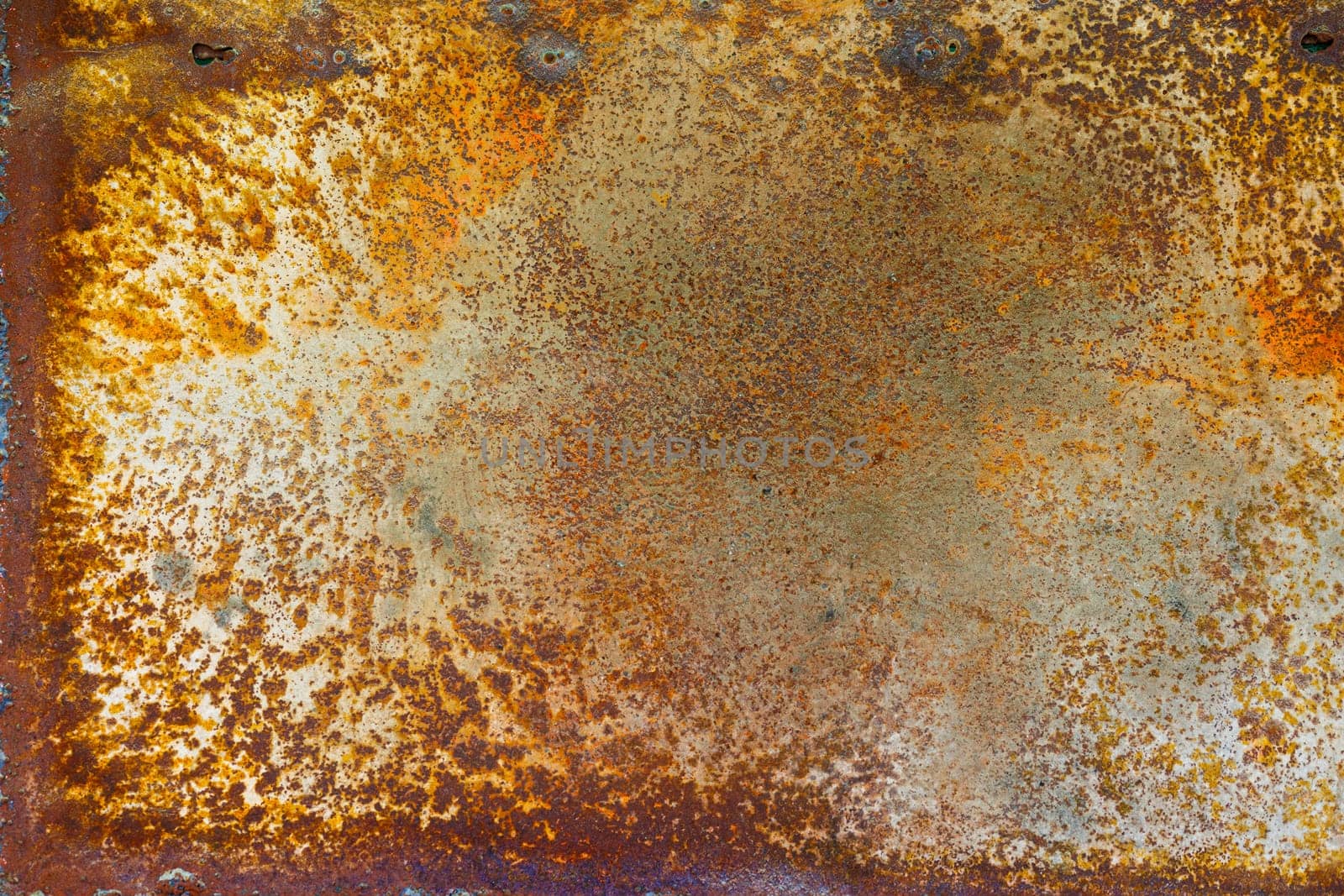Close up of a brownish rusted sheet metal surface with yellowish and orange hue and amber patina.