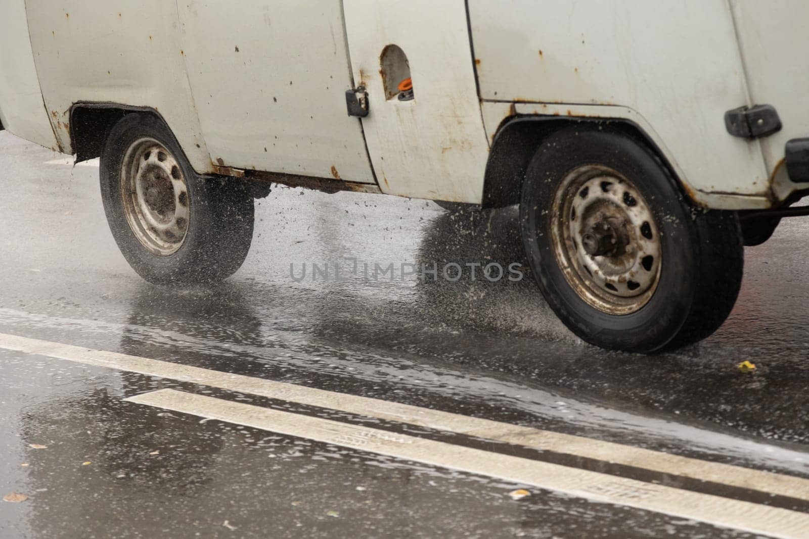 old rusty soviet minivan driving on the wet asphalt road during heavy rain by z1b