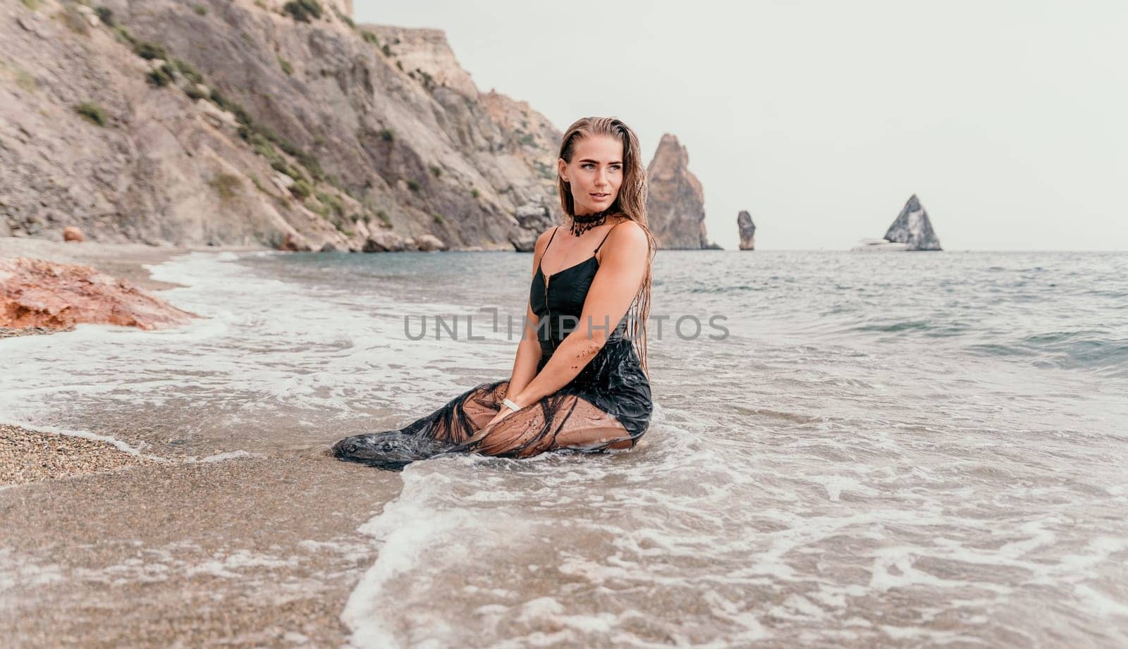 Woman summer travel sea. Happy tourist in black dress enjoy taking picture outdoors for memories. Woman traveler posing on sea beach surrounded by volcanic mountains, sharing travel adventure journey by panophotograph