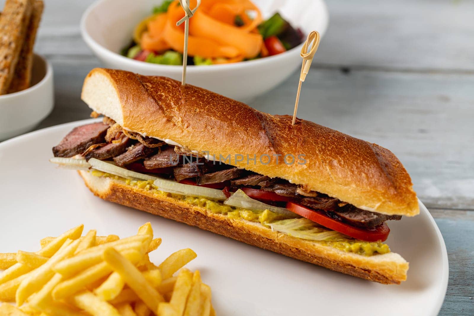 Grilled steak sandwich with french fries on a white porcelain plate