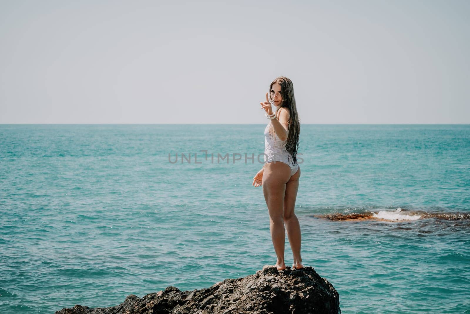 Woman sea yoga. Back view of free calm happy satisfied woman with long hair standing on top rock with yoga position against of sky by the sea. Healthy lifestyle outdoors in nature, fitness concept. by panophotograph