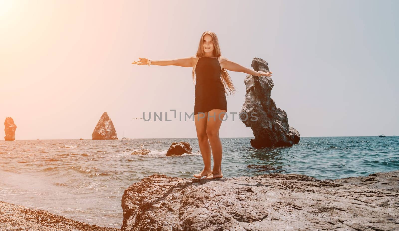 Woman travel sea. Young Happy woman in a long red dress posing on a beach near the sea on background of volcanic rocks, like in Iceland, sharing travel adventure journey