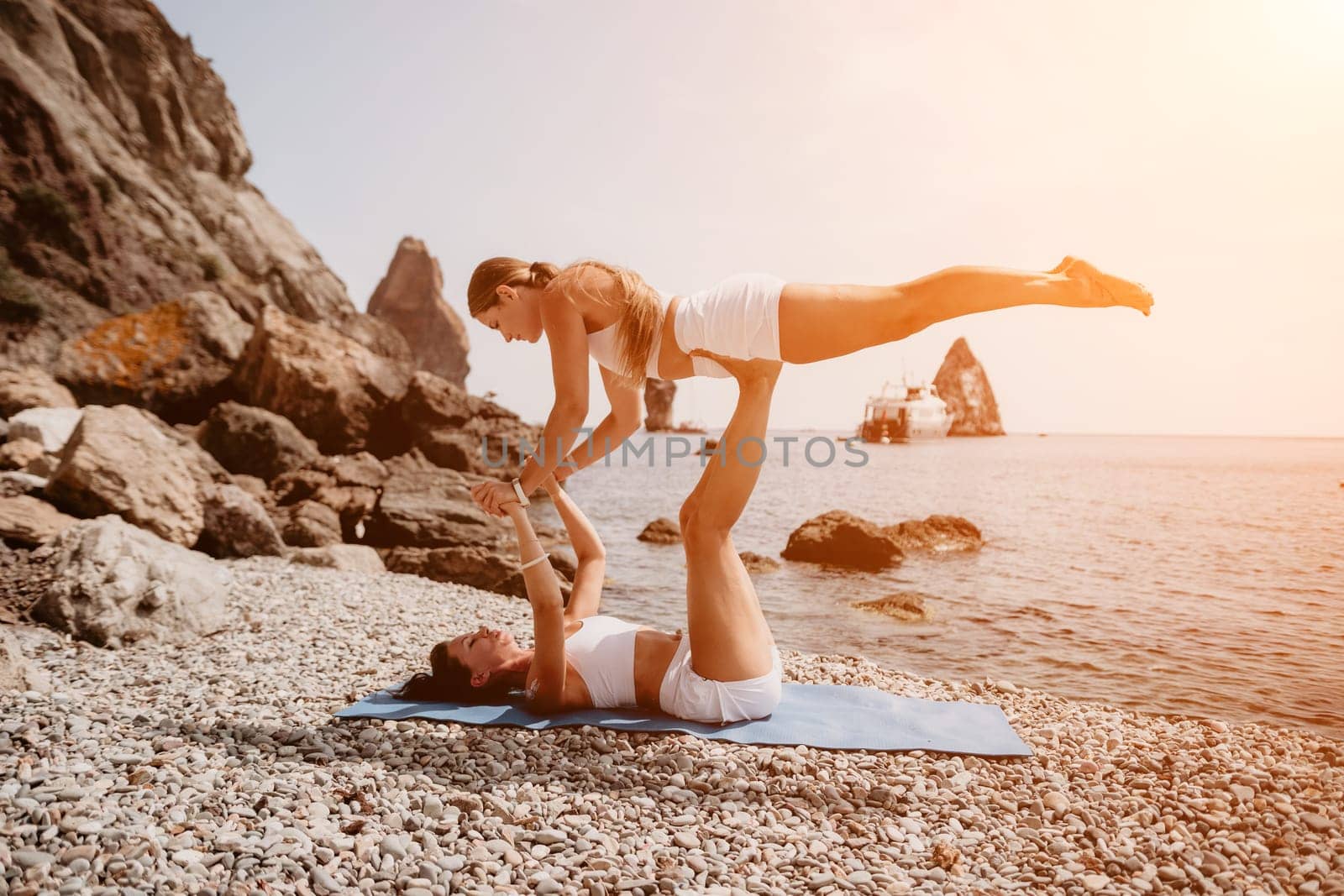 Woman sea yoga. Two happy women practicing yoga on the beach with ocean and rock mountains. Motivation and inspirational fit and exercising. Healthy lifestyle outdoors in nature, fitness concept. by panophotograph