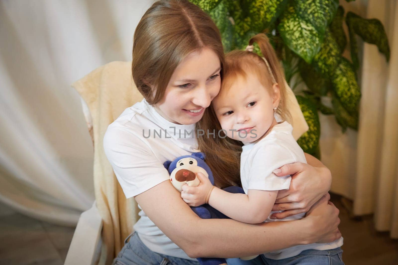 Happy loving family. Mother and daughter child girl playing and hugging in living room with wicker chair