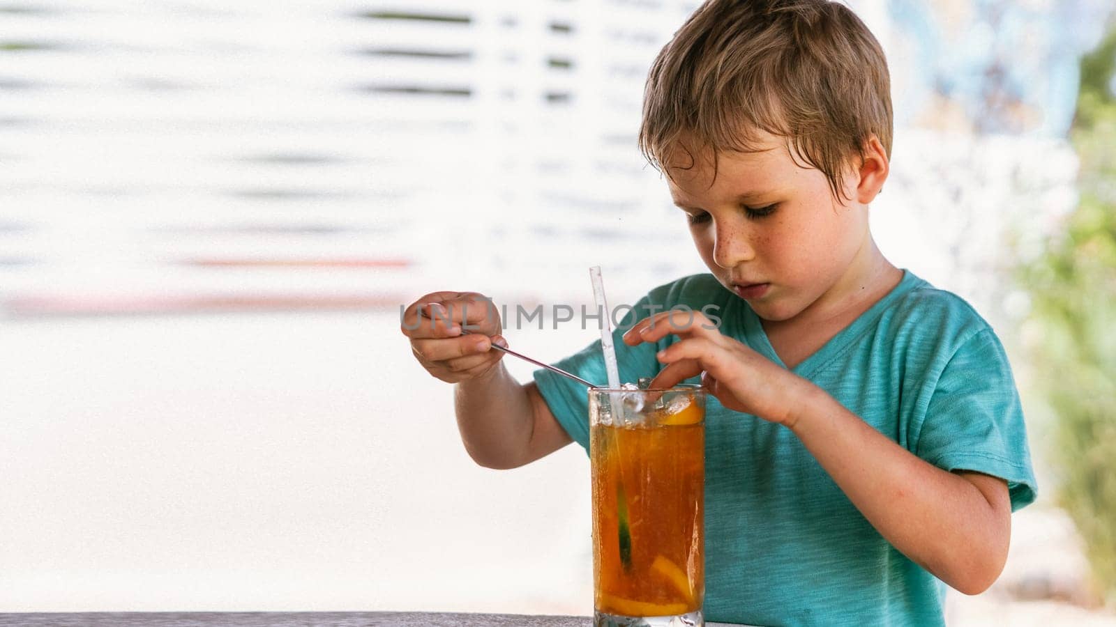 Happy childhood. Boy drinking fruit tea with ice in hot summer day time. Cute lover of sweets and tasty things.
