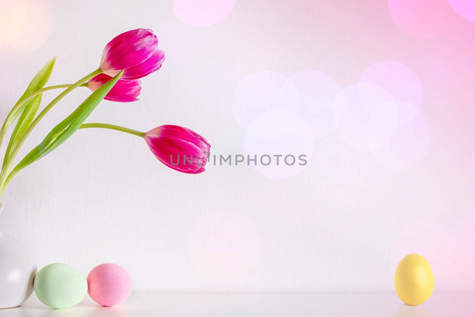 Spring pink tulip flowers with Easter eggs on pink background. Copy space