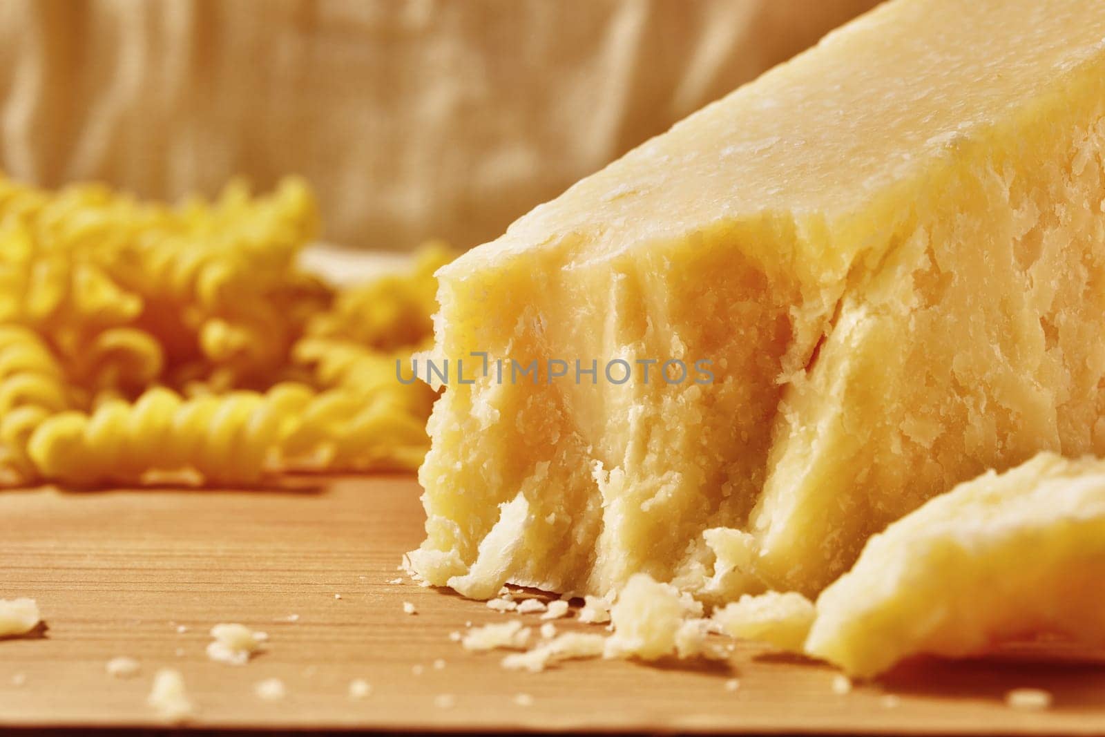 Italian hard cheese Parmesan -Parmigiano Reggiano produced from cow's milk on table , dry pasta in the background