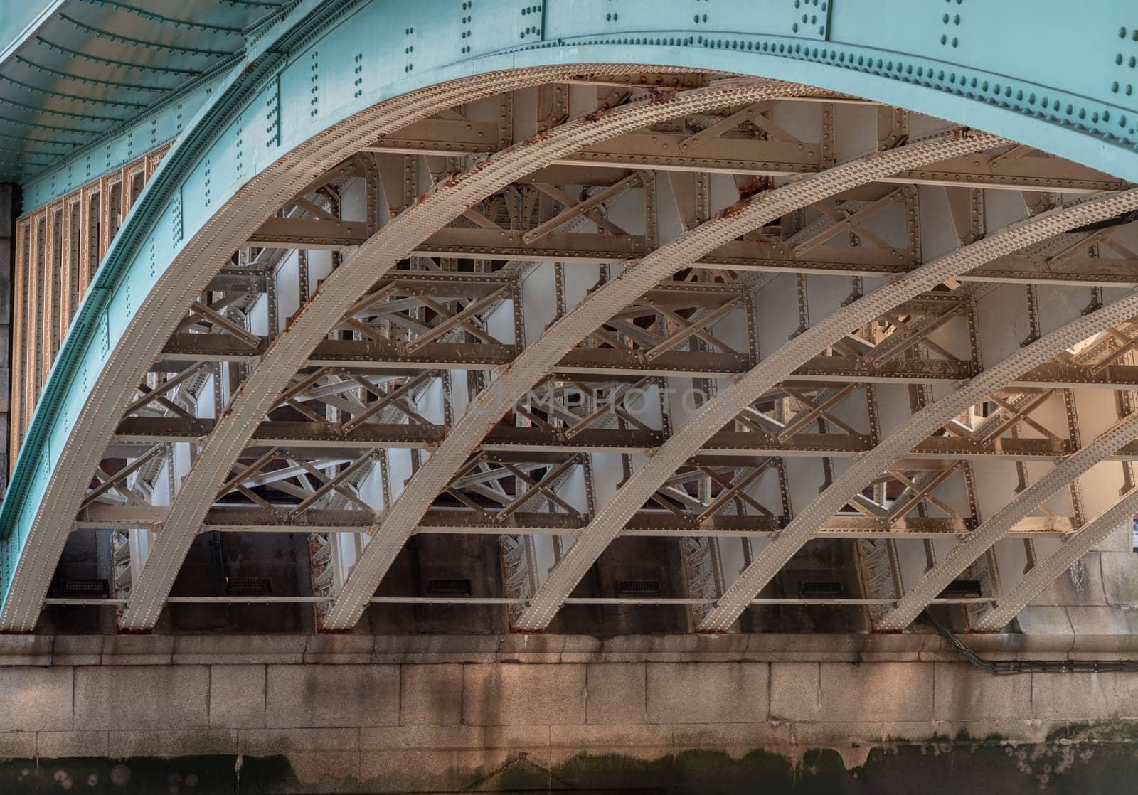 London, UK - Feb 27, 2024 - Detail of Structure and Girders supporting underneath Southwark Bridge Over The River Thames in London. The side of a turquoise cast iron bridge, Curved steel Bridge, Copy space, Selective focus.