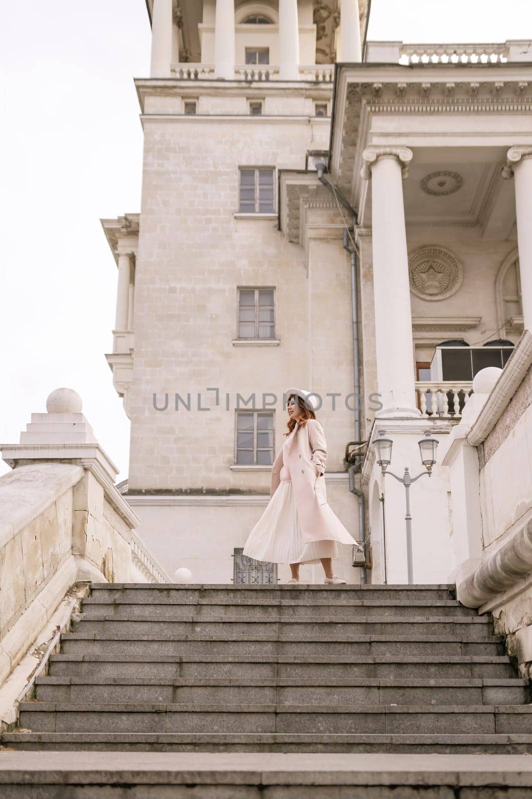 woman in elegant coat and hat against an intricate architectural backdrop, harmoniously blending modern fashion with historical allure. The soft daylight adds to its timeless appeal. by Matiunina