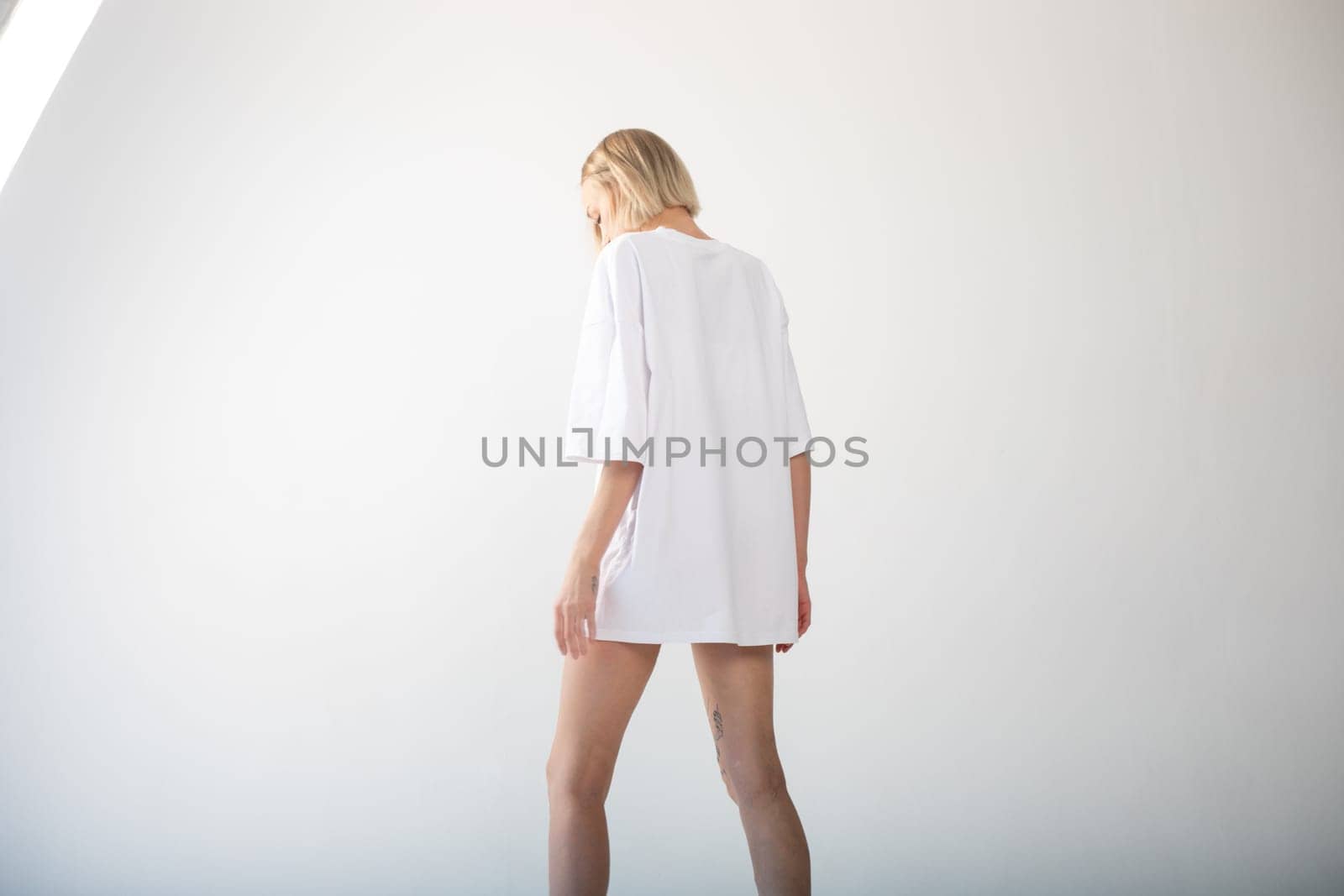 Beautiful girl in a white oversized t-shirt posing on a white background. High quality photo