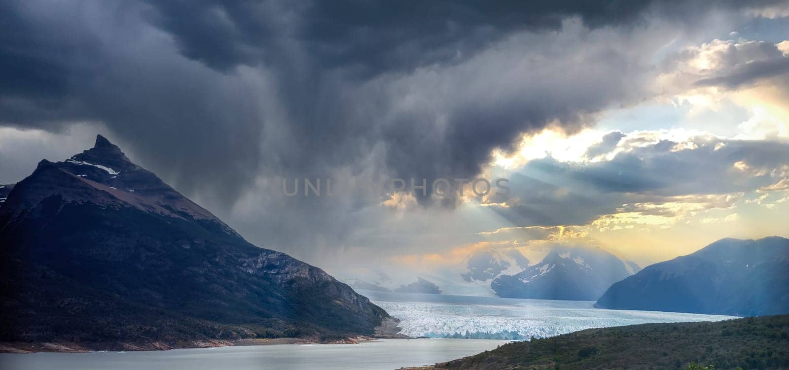 Dramatic glacier view with a mountain and dark clouds parting for sunlight.