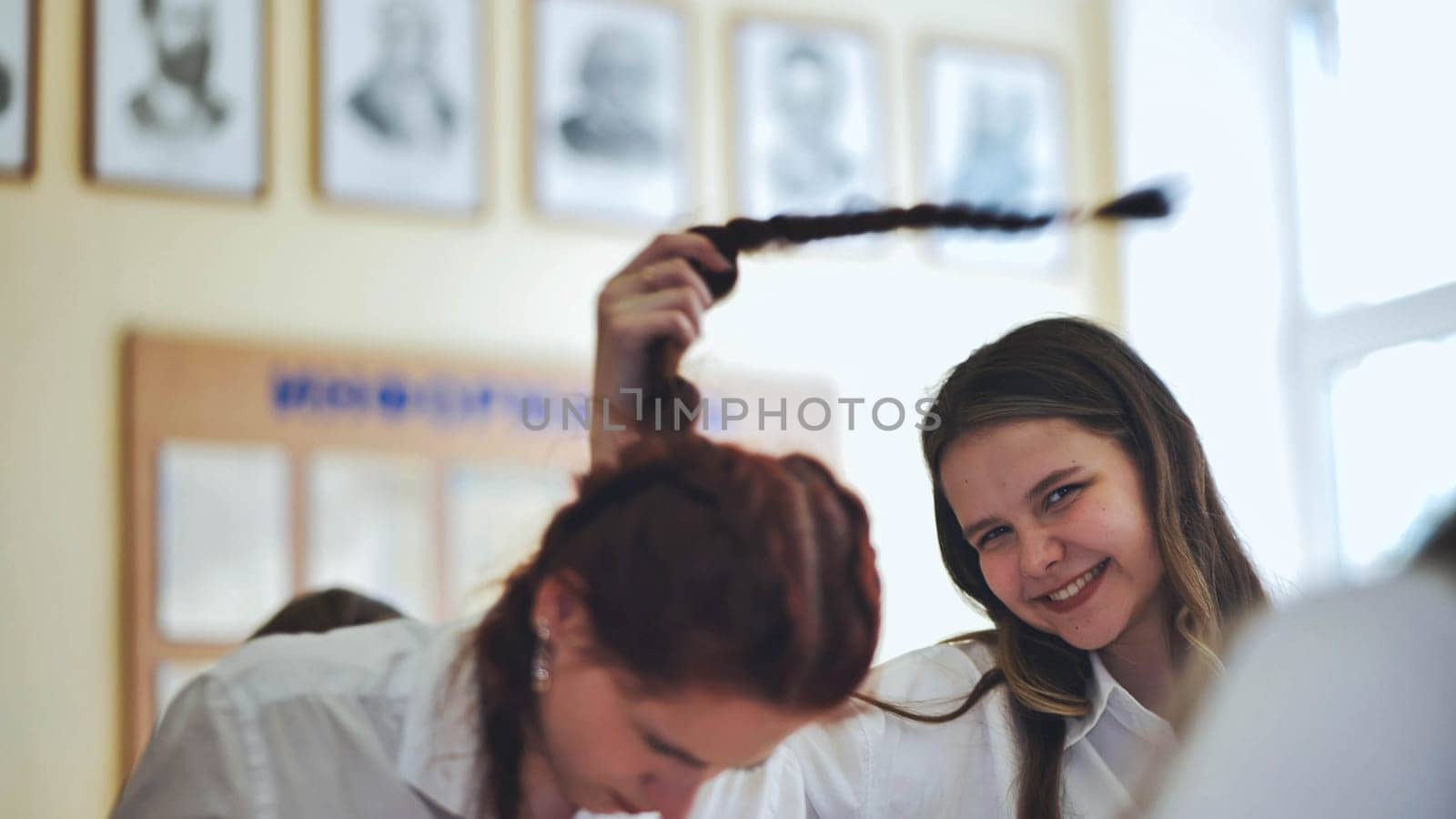 Fun schoolgirls in the classroom. Girl playing with her friend's pigtail