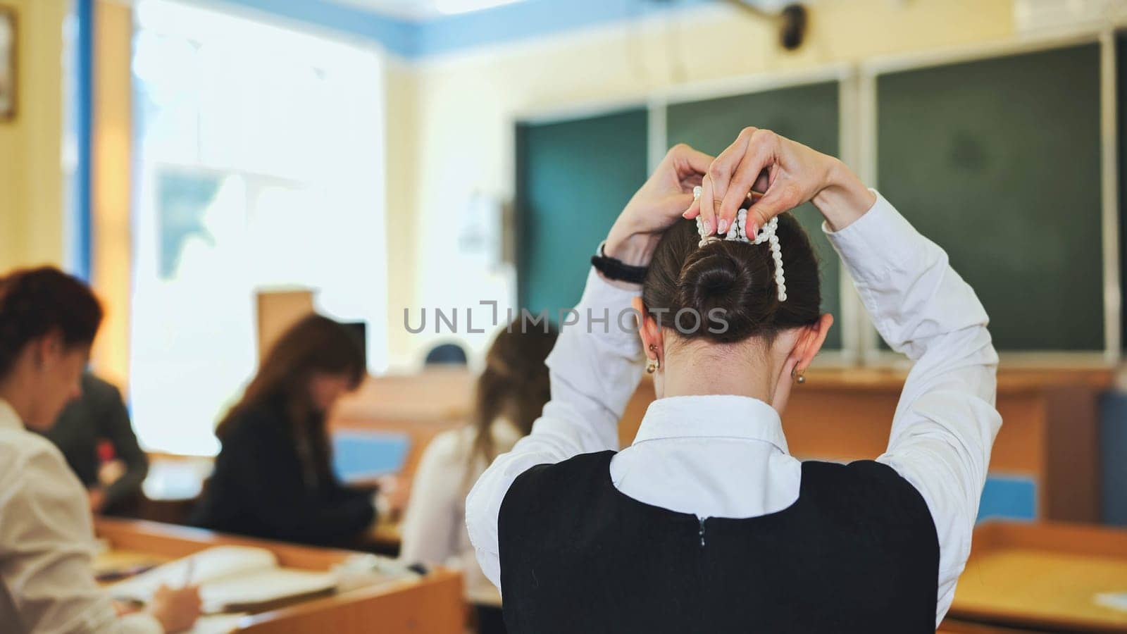 A schoolgirl fixes her hair during class. by DovidPro