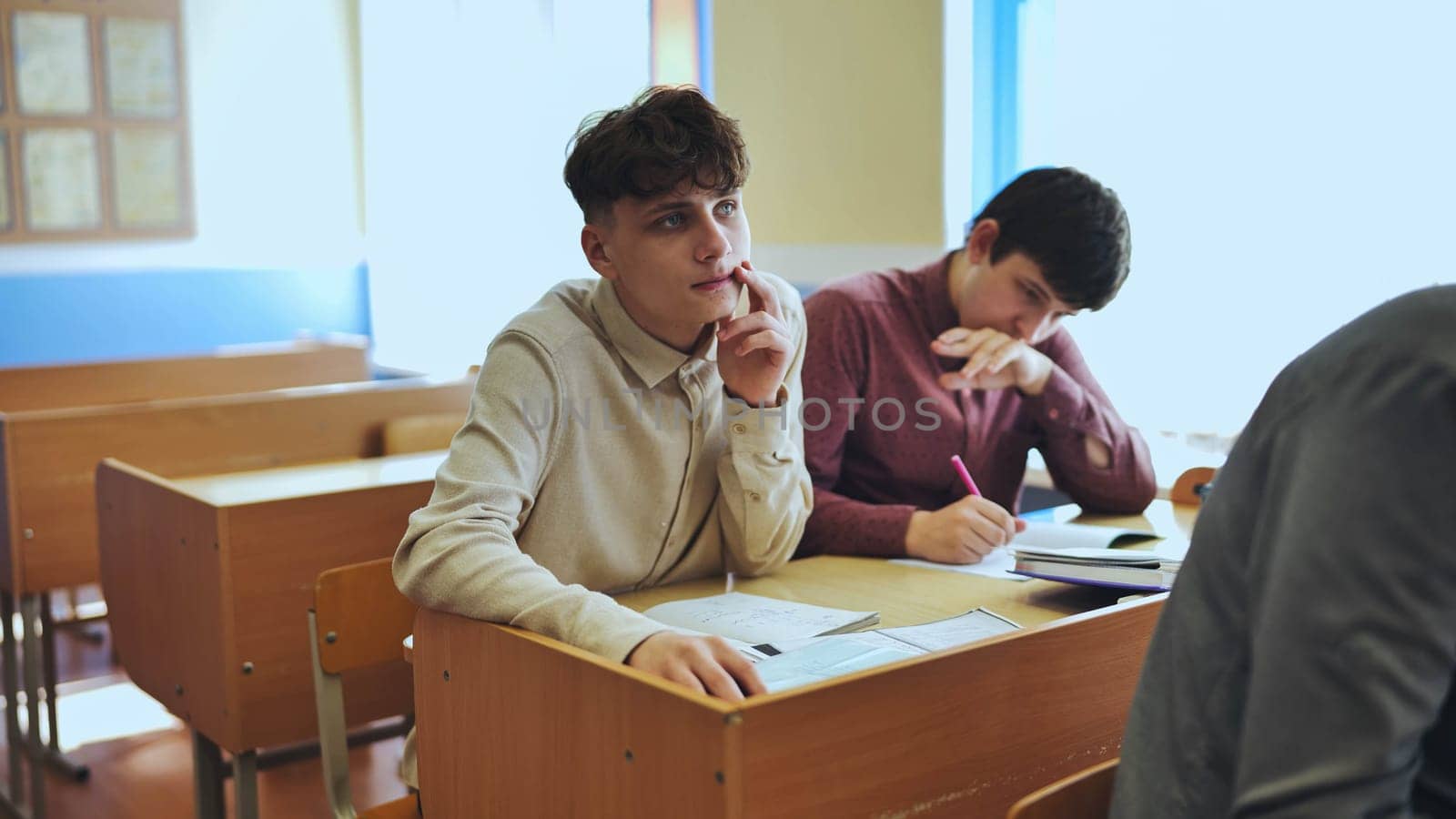 Schoolboys at a desk during class. The boy eats an apple. by DovidPro