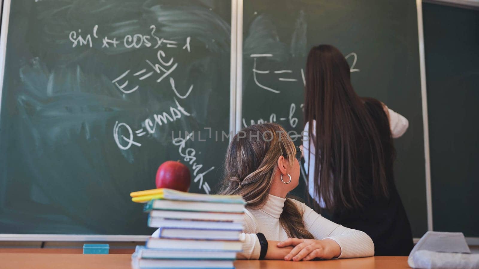 Two high school girls at the blackboard in their class. by DovidPro